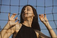 一名女子在户外的排球网后摆姿势，拥抱无忧无虑的夏日氛围