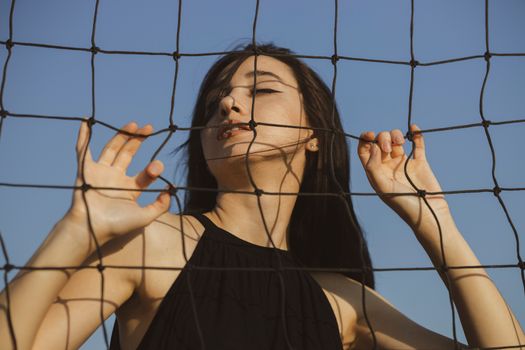 一名女子在户外的排球网后摆姿势，拥抱无忧无虑的夏日氛围