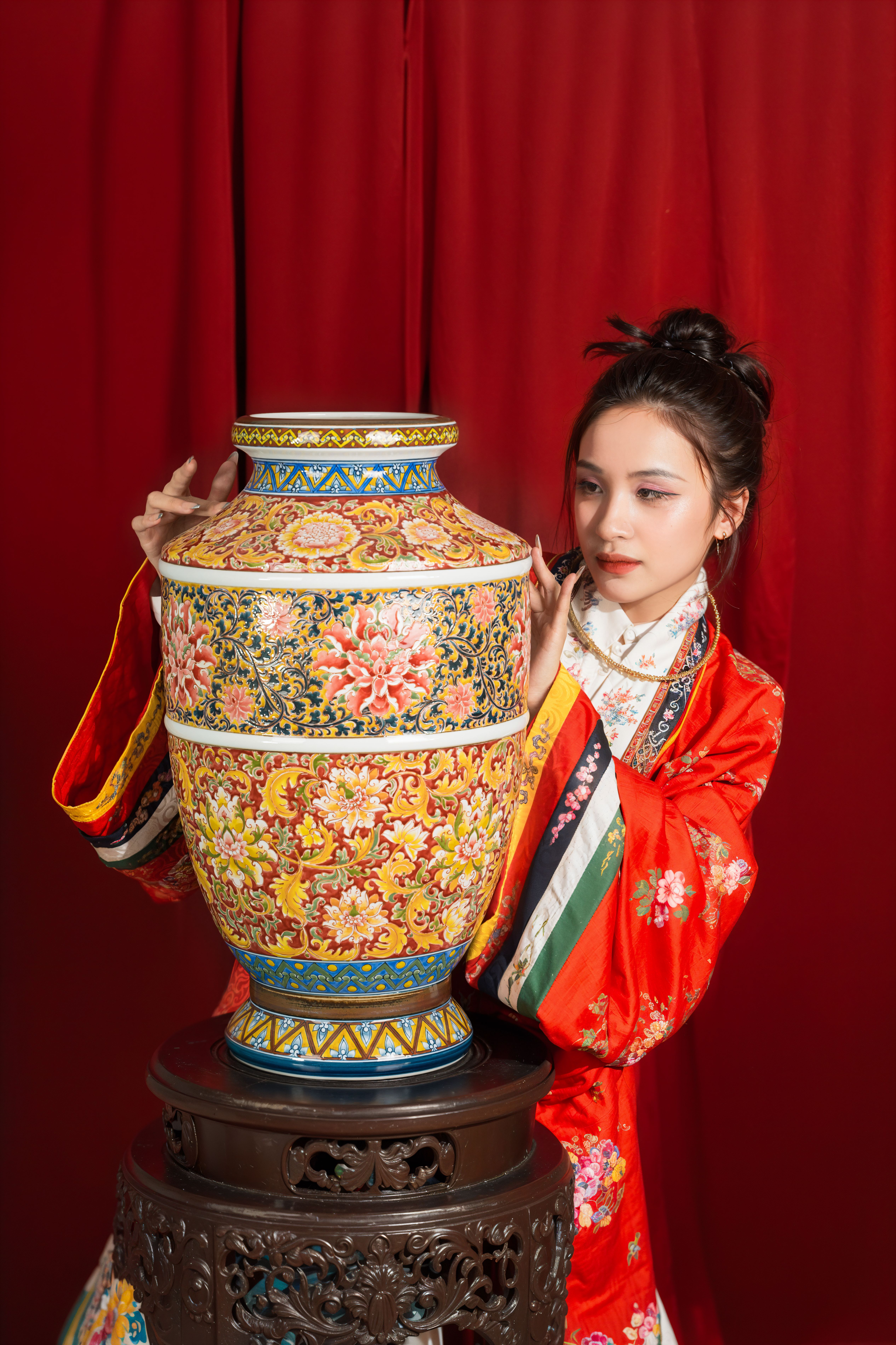 Woman in traditional attire examining a colorful Chinese vase against a red backdrop.