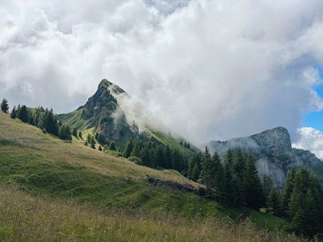 Breathtaking view of rugged alpine peaks surrounded by lush greenery and dramatic clouds.