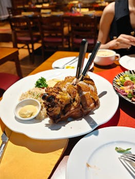 Delicious crispy pork knuckle with mustard, rice, and salad served in an ambient restaurant setting.