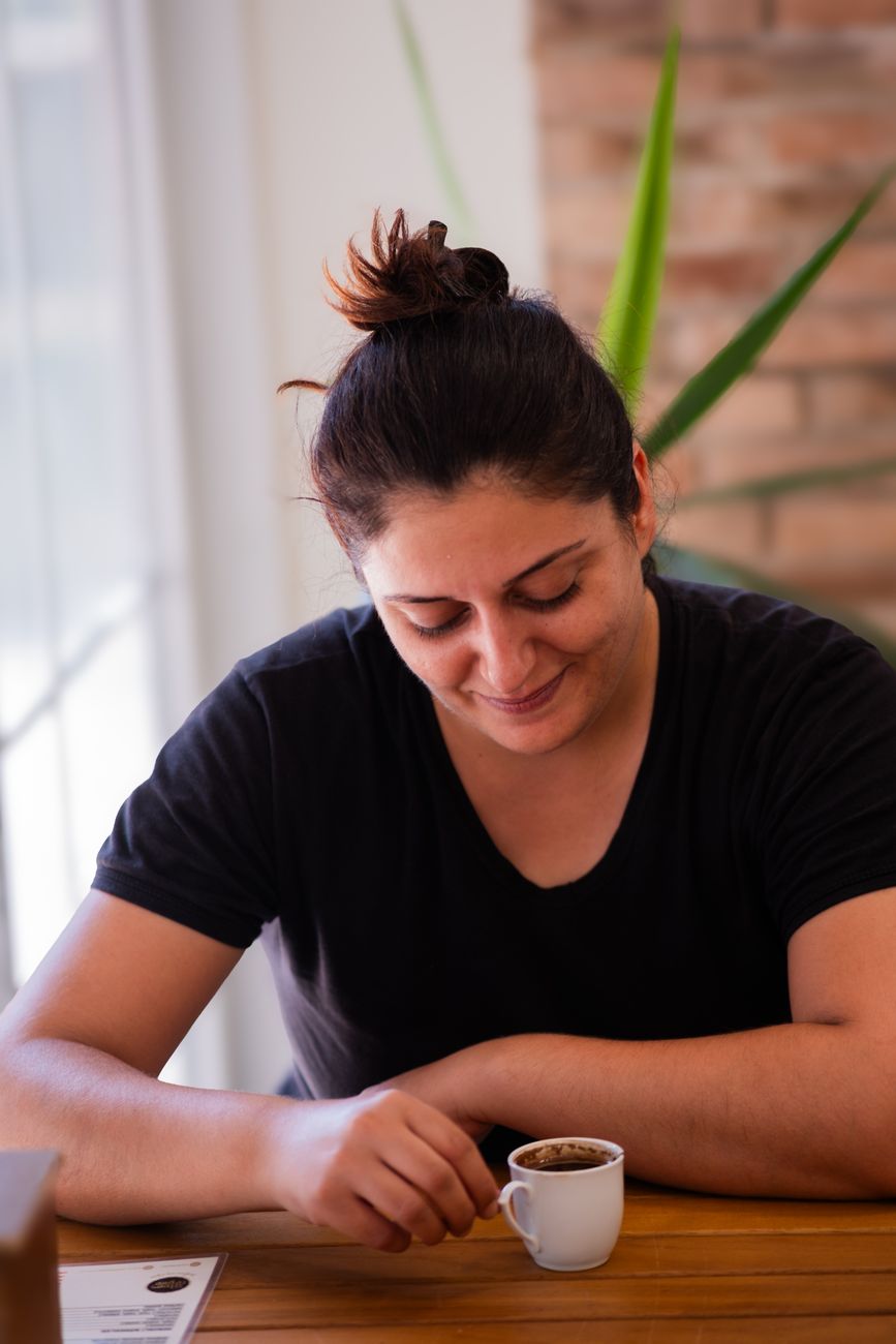 A woman savoring a coffee at a cozy cafe in İzmir, Türkiye, captured in a candid moment.