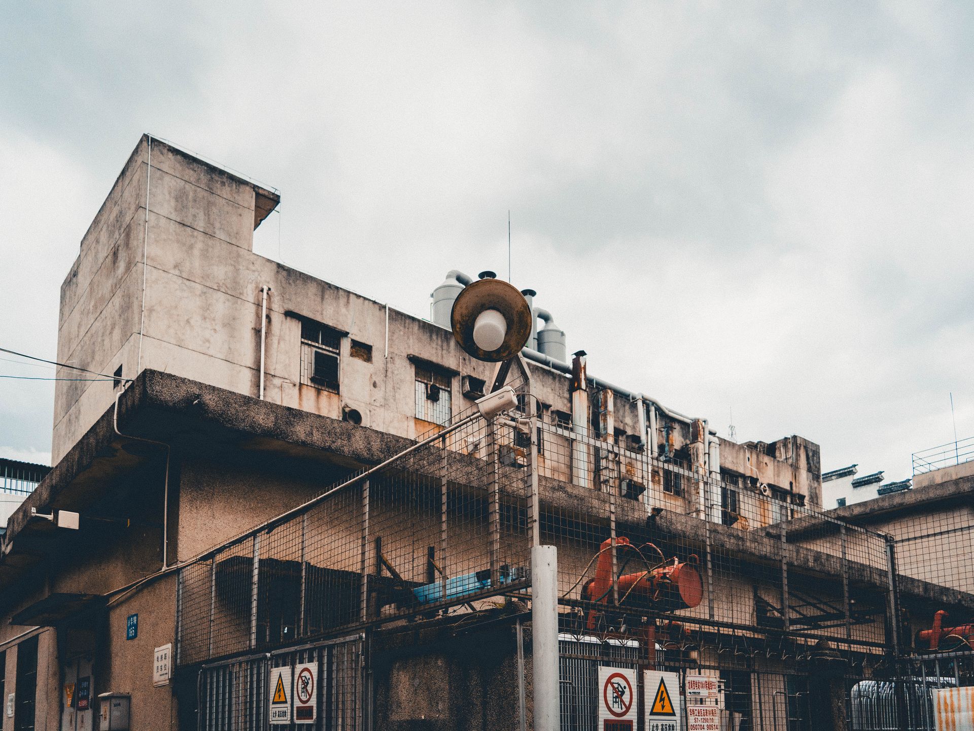 Exterior of an old industrial building with alarms and warning signs against a cloudy sky.