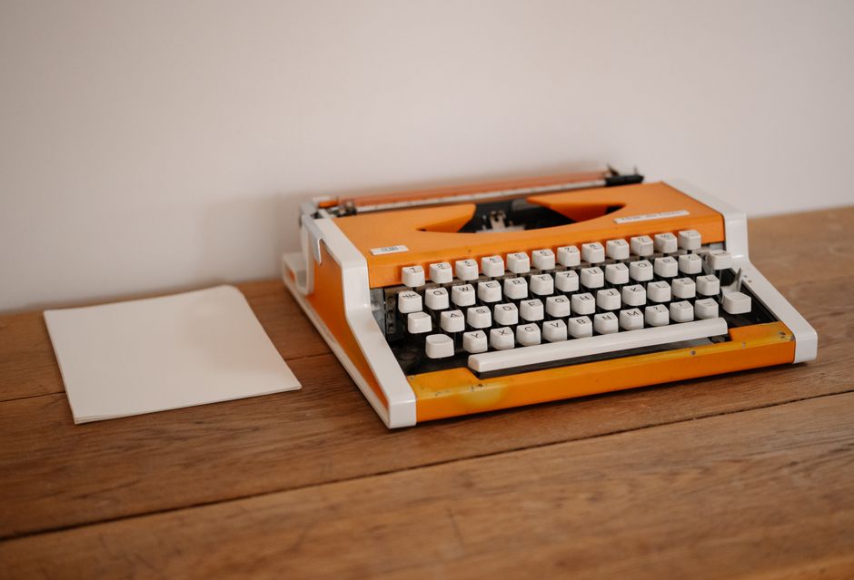Retro orange typewriter on a wooden desk with a blank sheet of paper, perfect for nostalgic and creative concepts.
