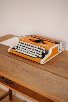 Retro orange typewriter placed on a rustic wooden desk in a minimalist setting.