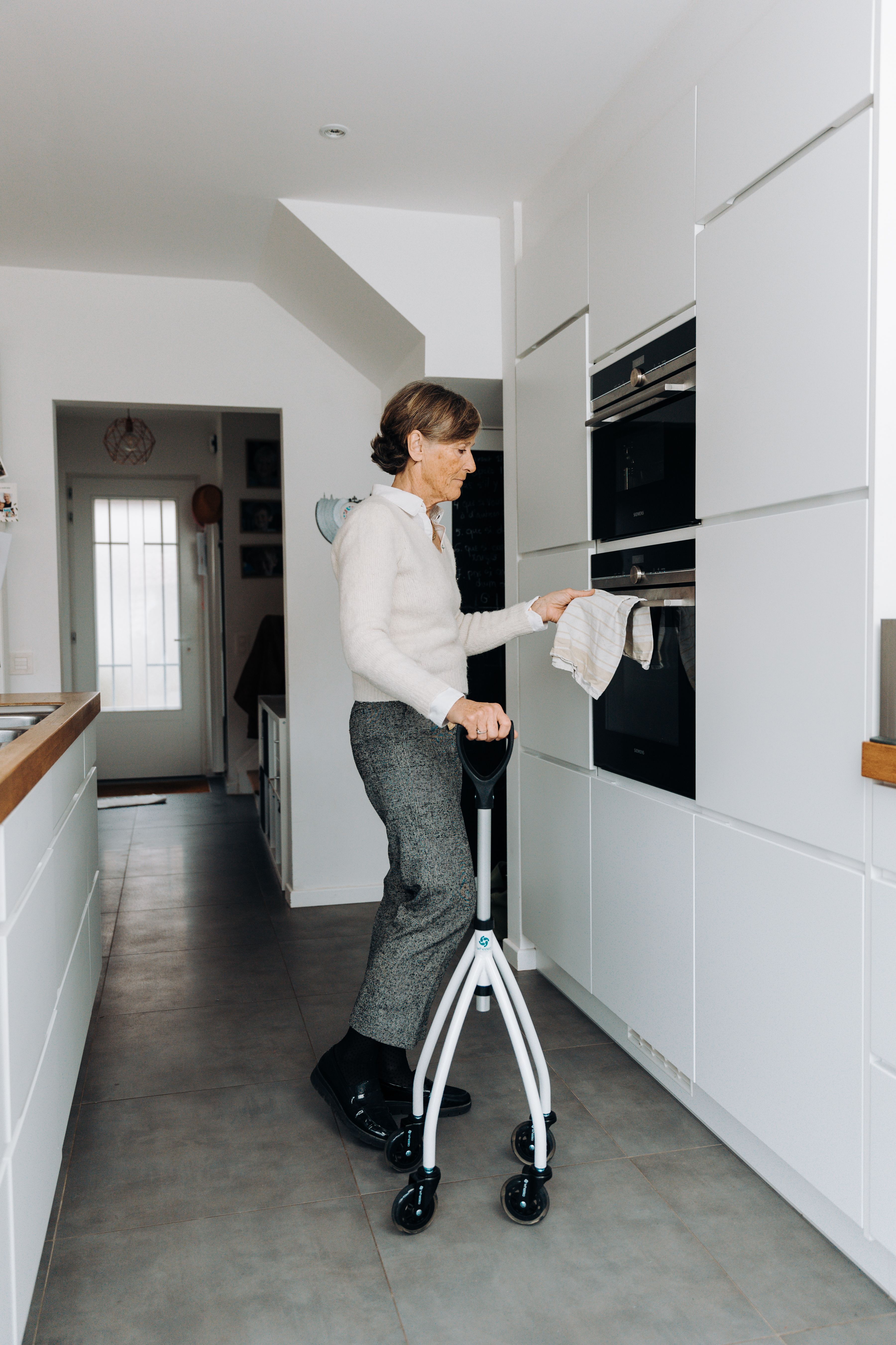 Elderly woman with walker accessing oven, showcasing independence and accessibility in a modern kitchen setting.