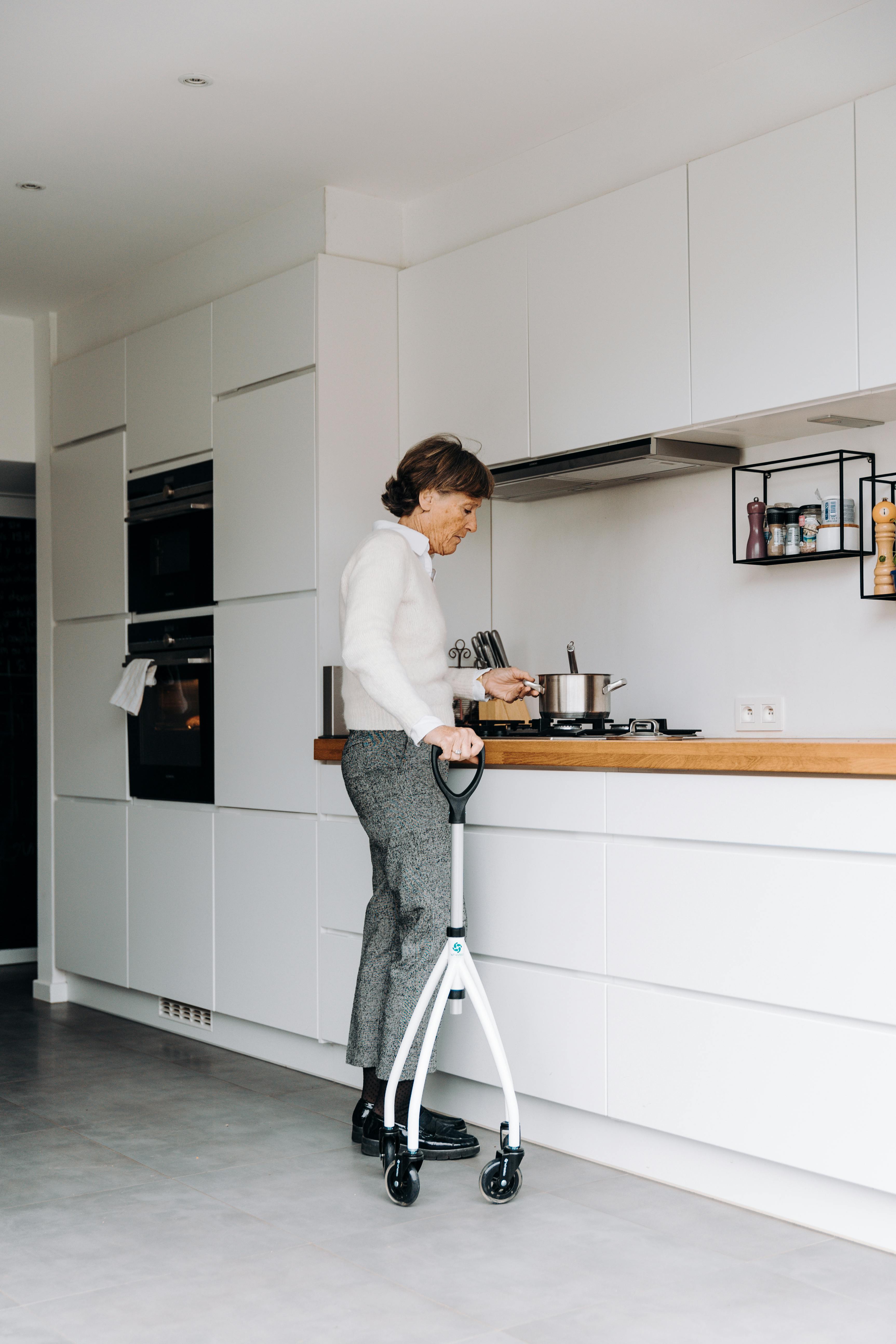 Elderly woman using walker while cooking in a sleek, modern kitchen interior.