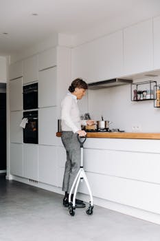 Elderly woman using walker while cooking in a sleek, modern kitchen interior.
