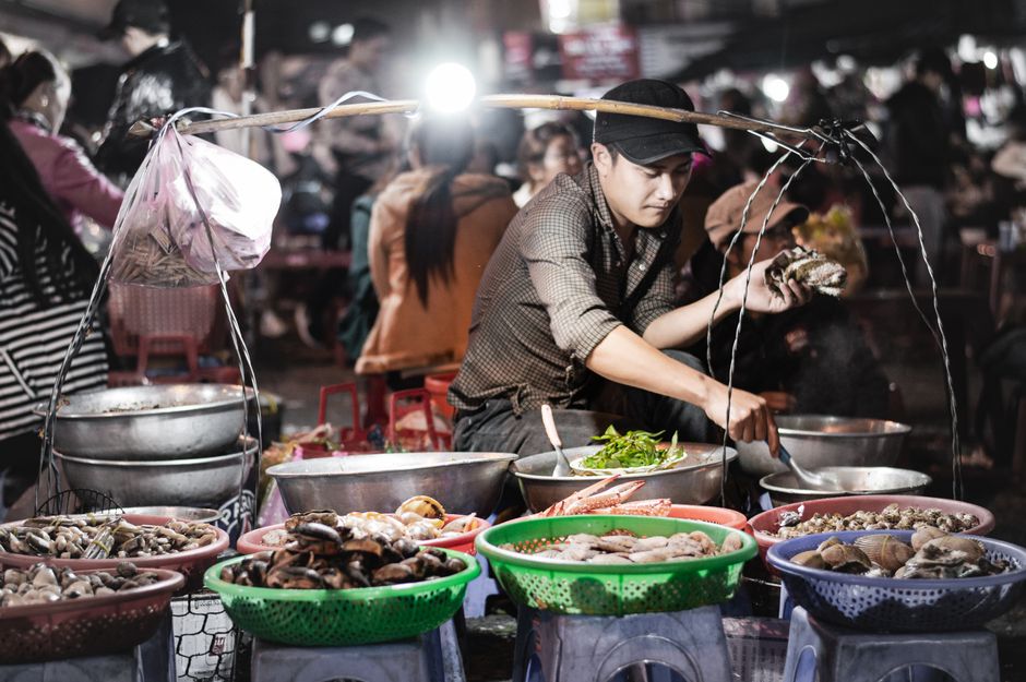 A vibrant street food scene in Mong Cai, Vietnam, with local seafood dishes, bustling market atmosphere, colorful signage, morning light, highly detailed documentary travel photography