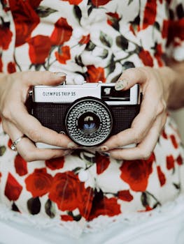 Close-up of hands holding a vintage Olympus Trip 35 camera against a floral blouse.