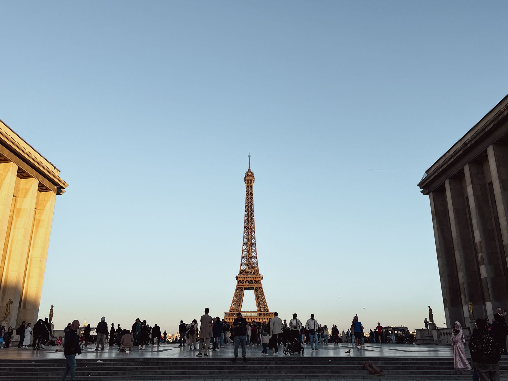 Tourists gathered below the Eiffel Tower at twilight, a popular hour for visiting the Eiffel Tower in Paris