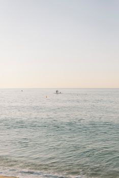 Calm ocean with paddleboarders under a serene sunset sky, perfect for peaceful moments.