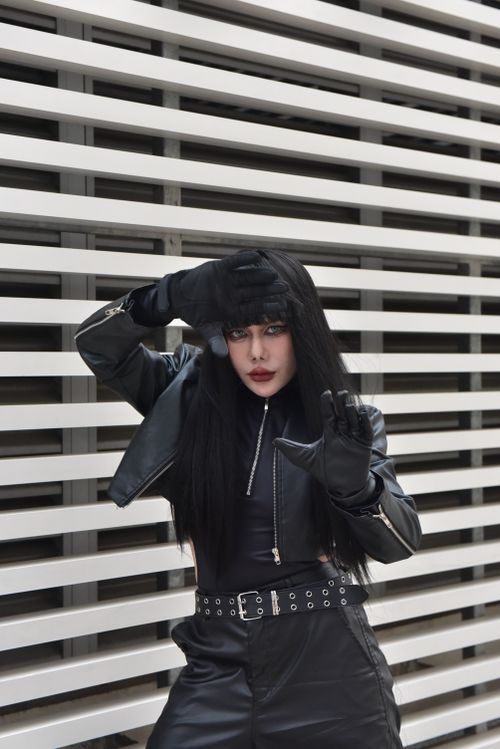 Free Fashionable woman in black leather outfit striking a bold pose against a modern wall. Stock Photo