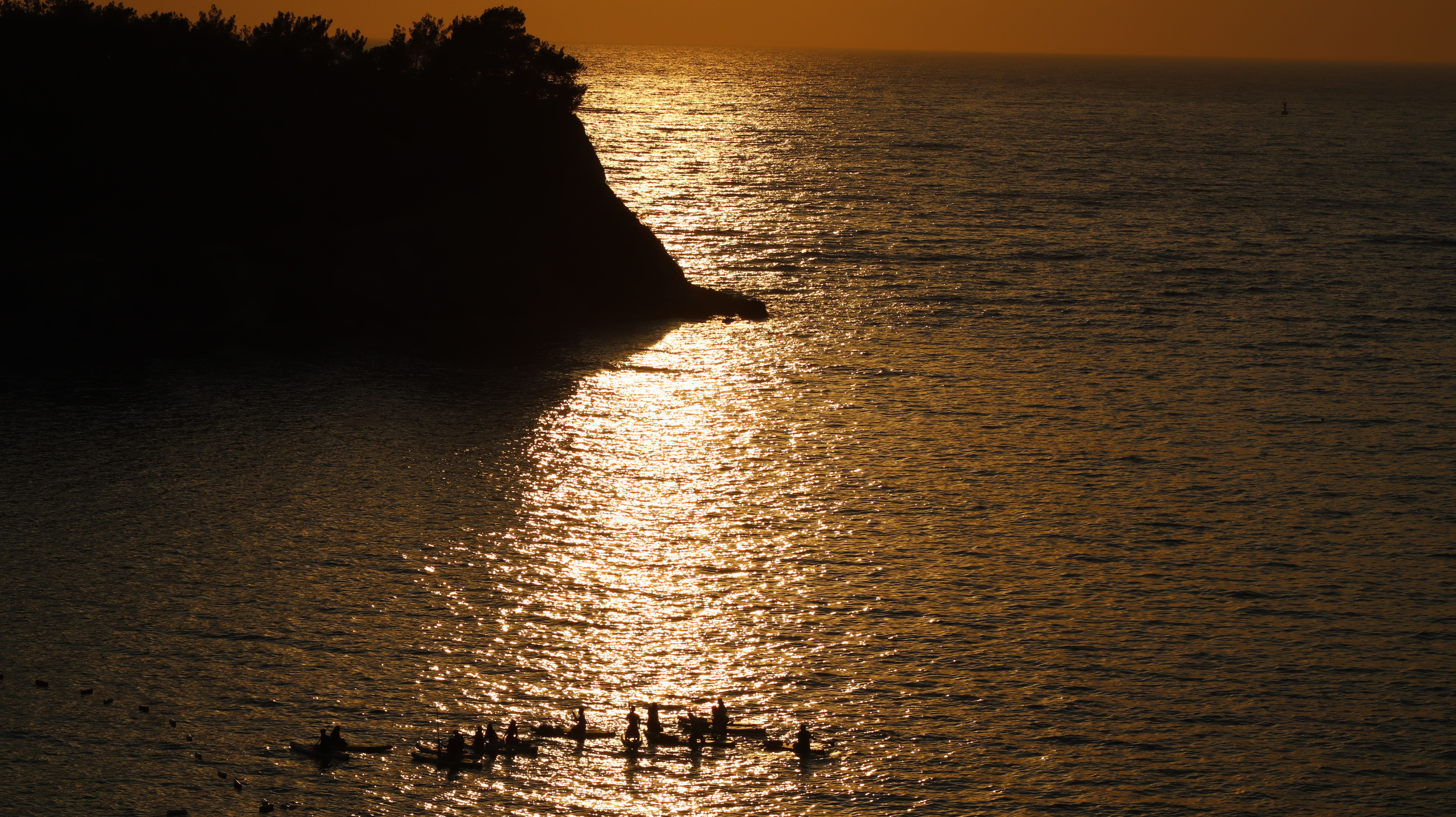 Sunset over Ocean with Silhouetted Cliff and Swimmers · Free Stock Photo