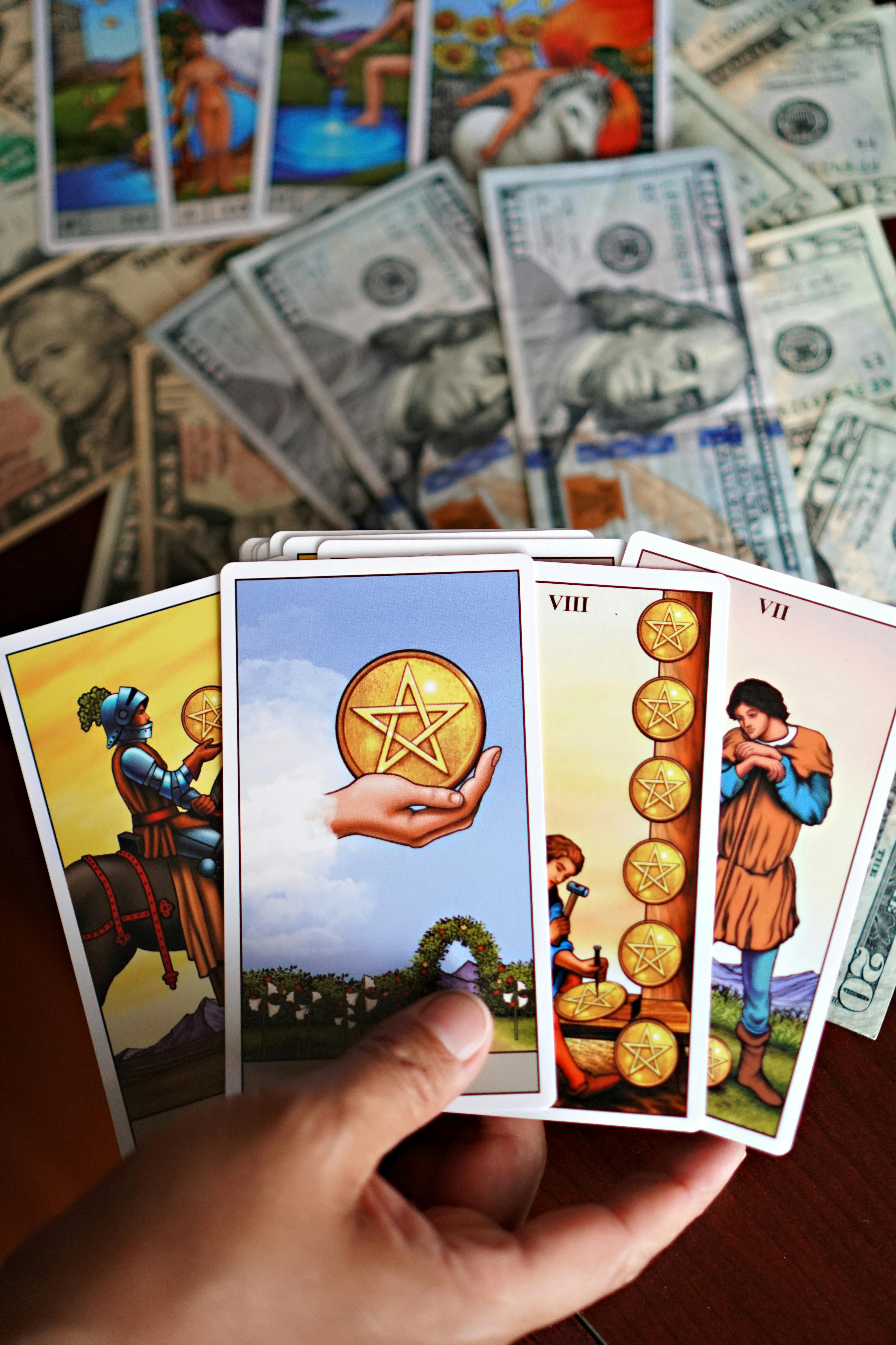 A hand holds tarot cards against a backdrop of US dollar bills.