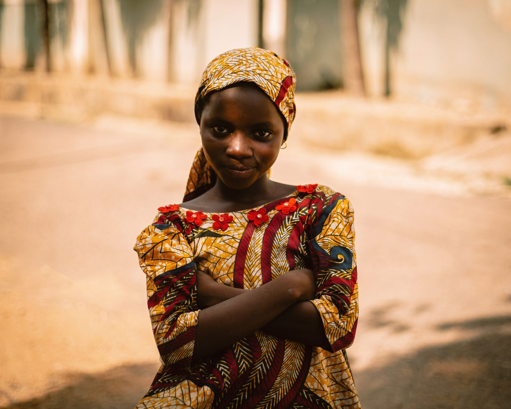A young girl in vibrant traditional Nigerian attire poses outdoors with confidence.