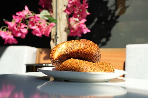 Free Delicious sesame seed bagels on a plate against vibrant pink flowers. Sunlit outdoor setting. Stock Photo