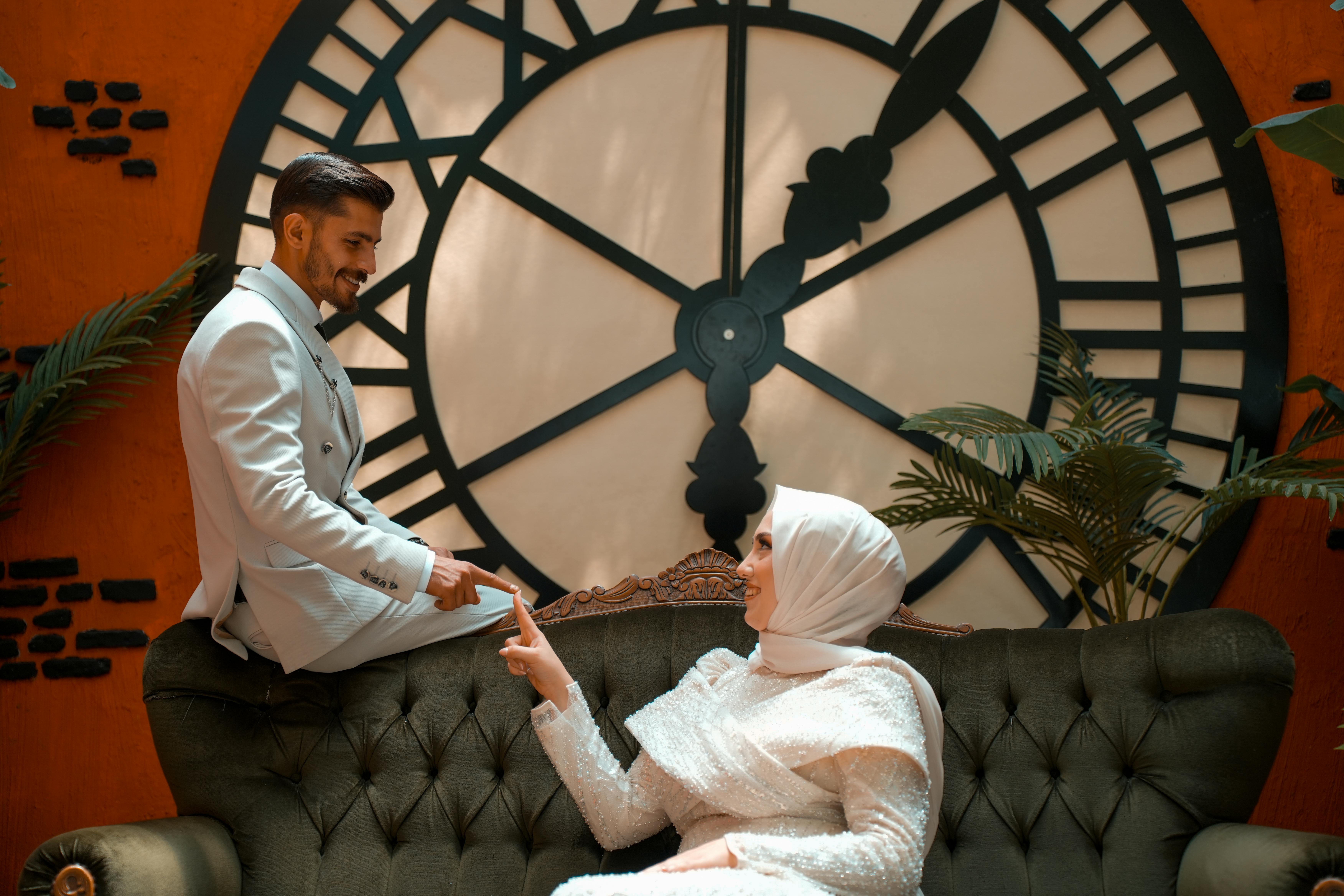 Free Stylish couple in formal attire enjoying a moment by a large vintage clock indoors. Stock Photo