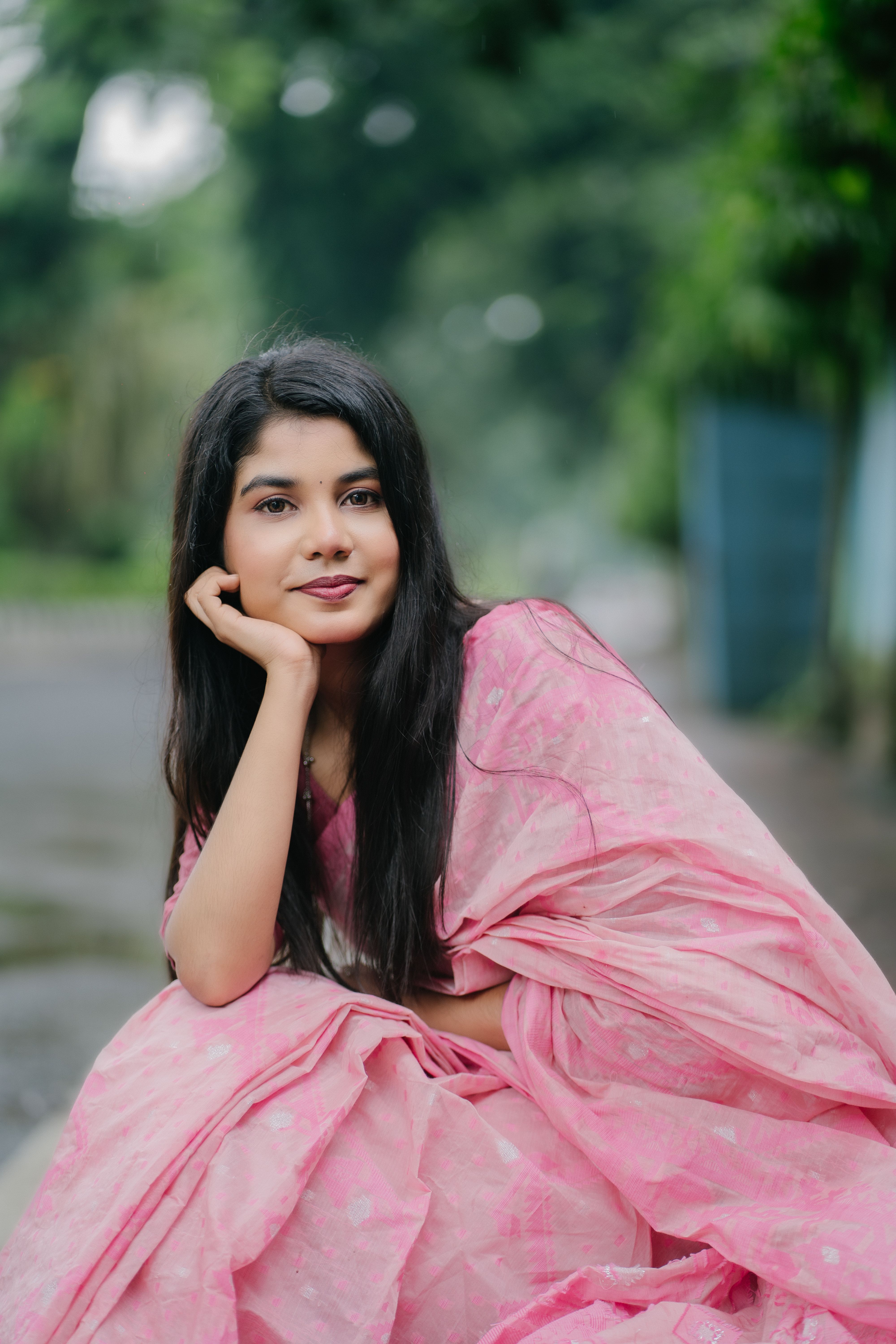 Smiling woman in pink saree posing outdoors on a serene day.