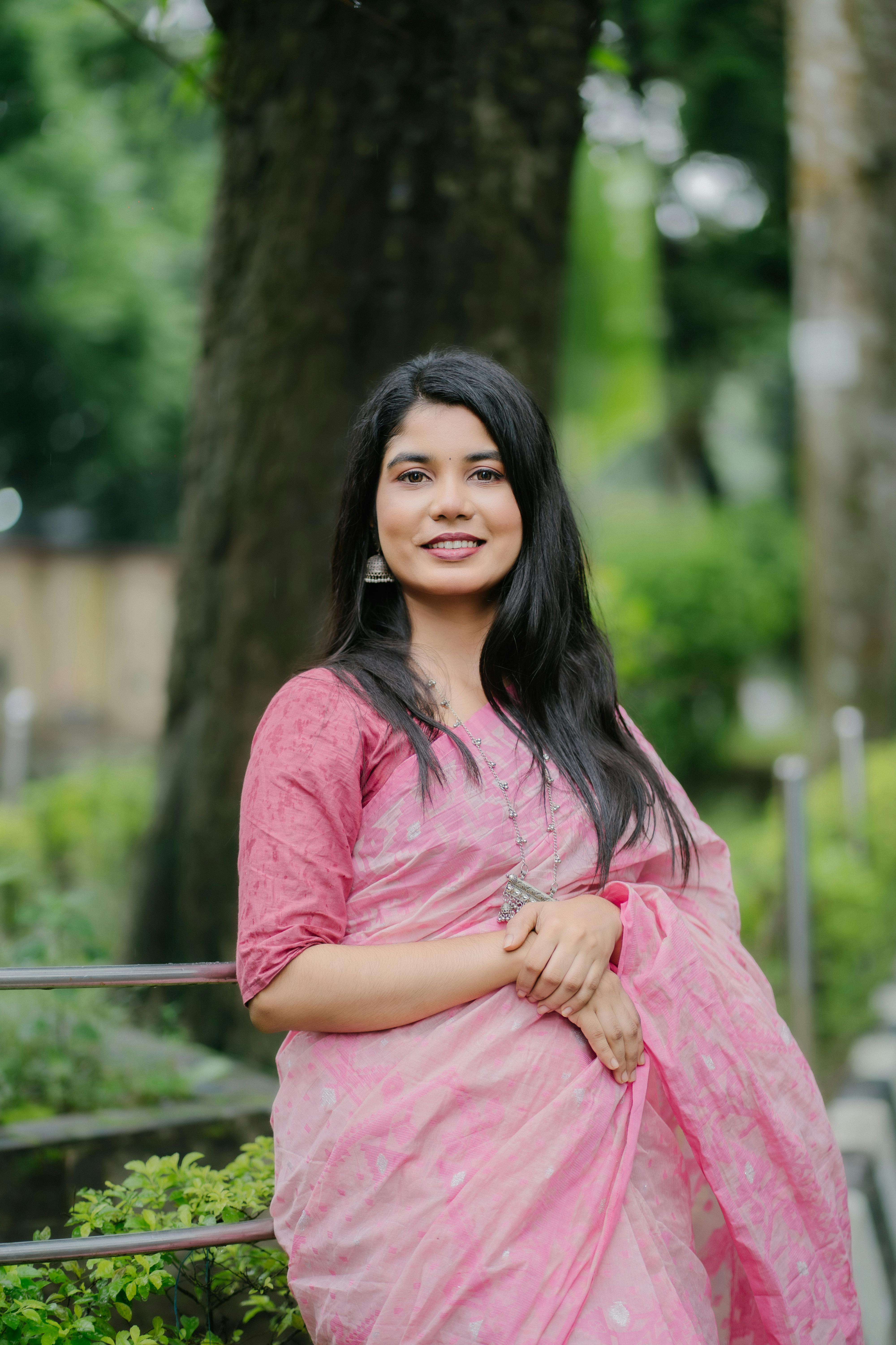 Elegant woman in pink saree smiling in a garden setting.