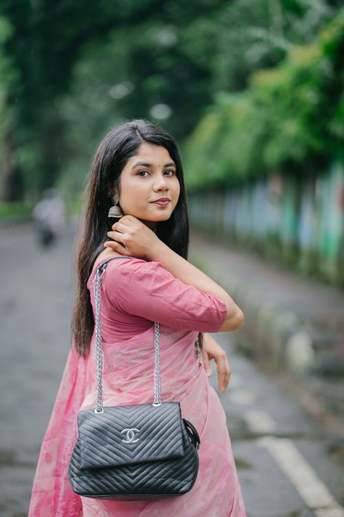 Free Stylish woman in pink saree posing outdoors with a black handbag, exuding elegance. Stock Photo