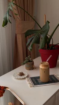 Inviting indoor setting with iced coffee, potted plant, and decor on a white table.