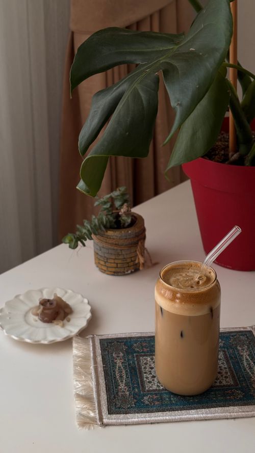 Free A cozy indoor scene with iced coffee, houseplants, and decorative mat. Stock Photo