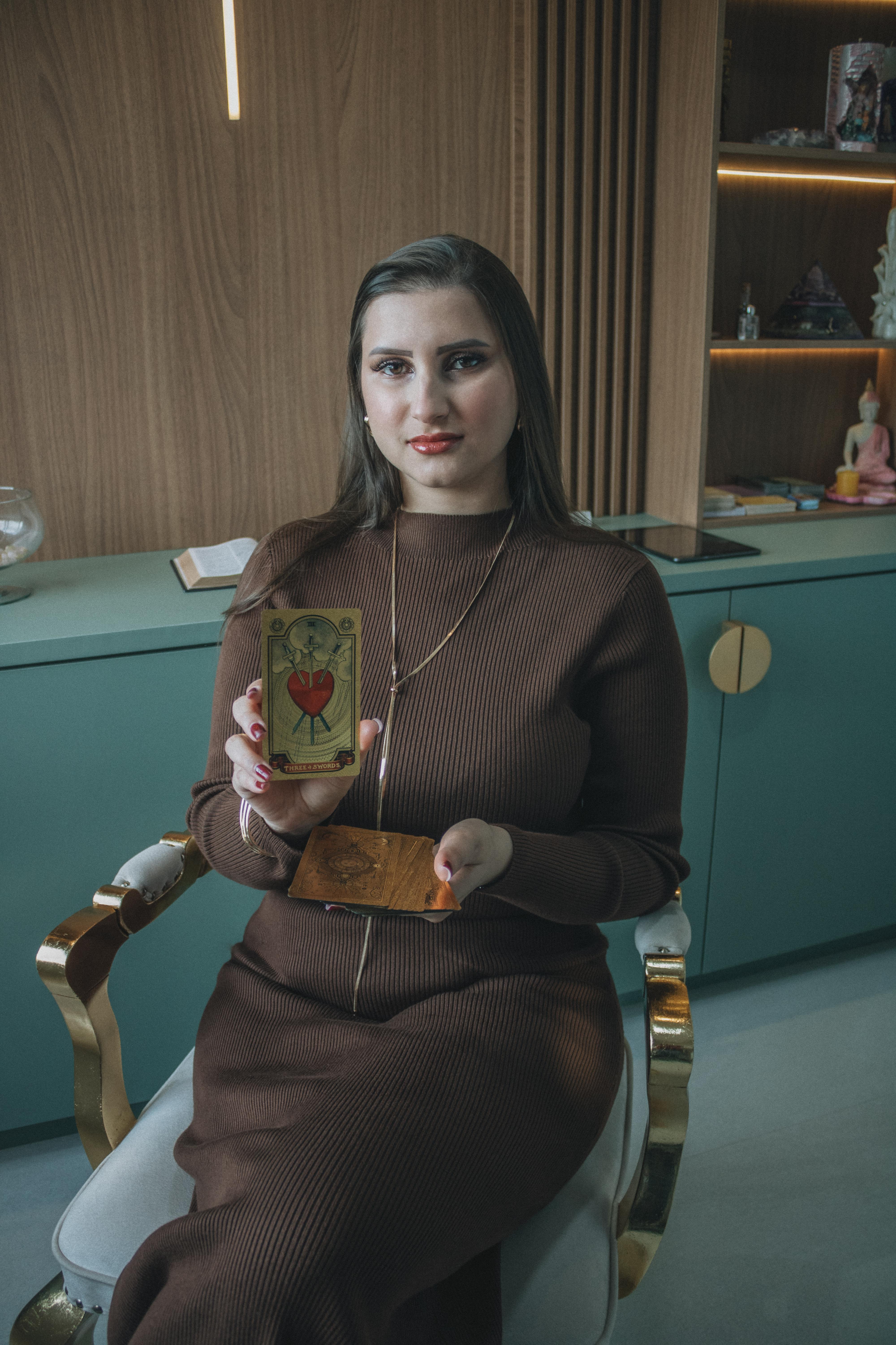 ingyenes Egy barna ruhás nő tarot kártyákat mutat be egy stílusos belső térben. Stockfotó