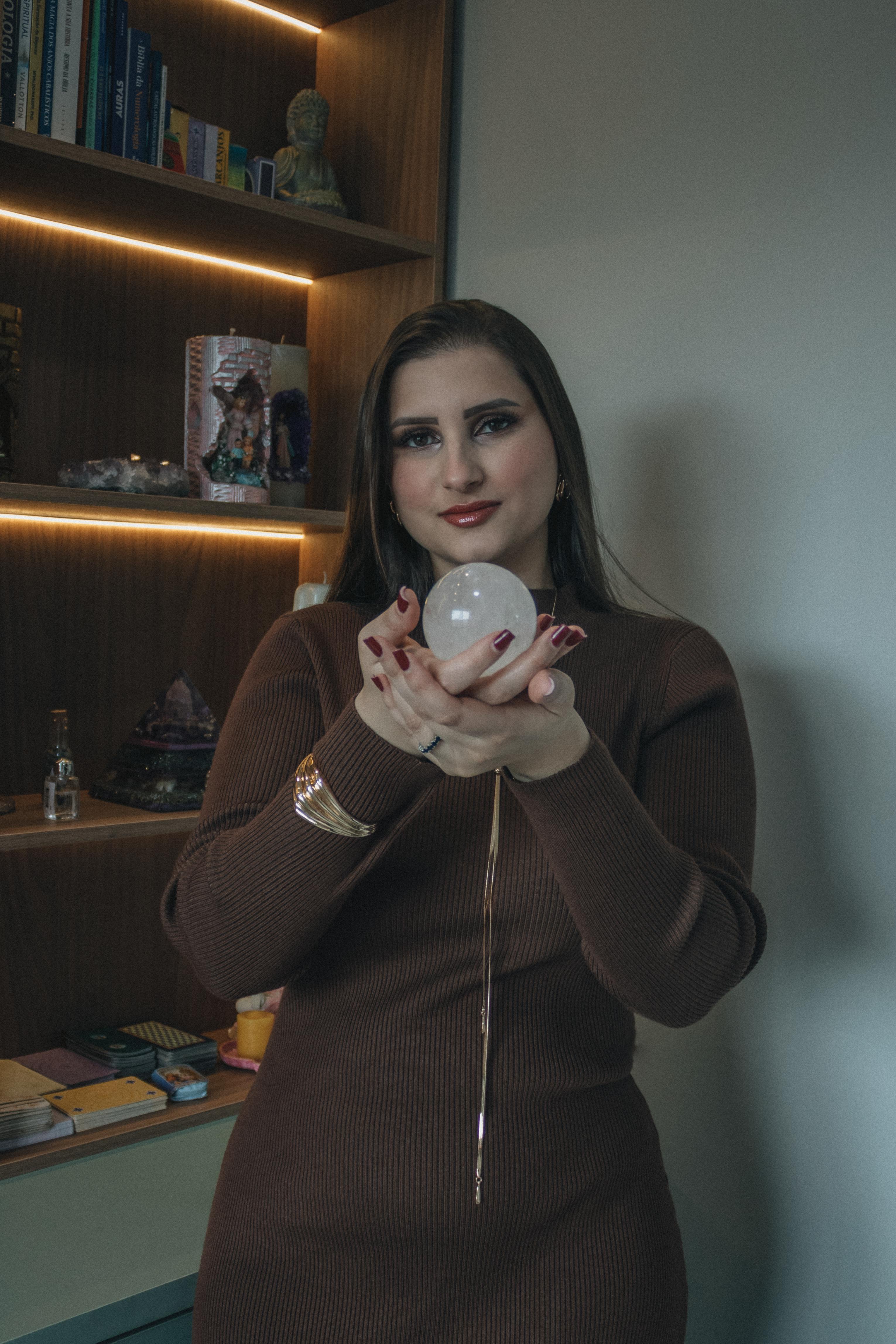 ingyenes Egy nő áll bent, kristálygömböt tartva a kezében, könyvek és polcok veszik körül, misztikus hangulatot árasztva. Stockfotó