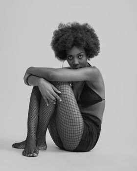 Artistic black and white portrait of a woman in fishnet tights, seated in a contemplative pose.