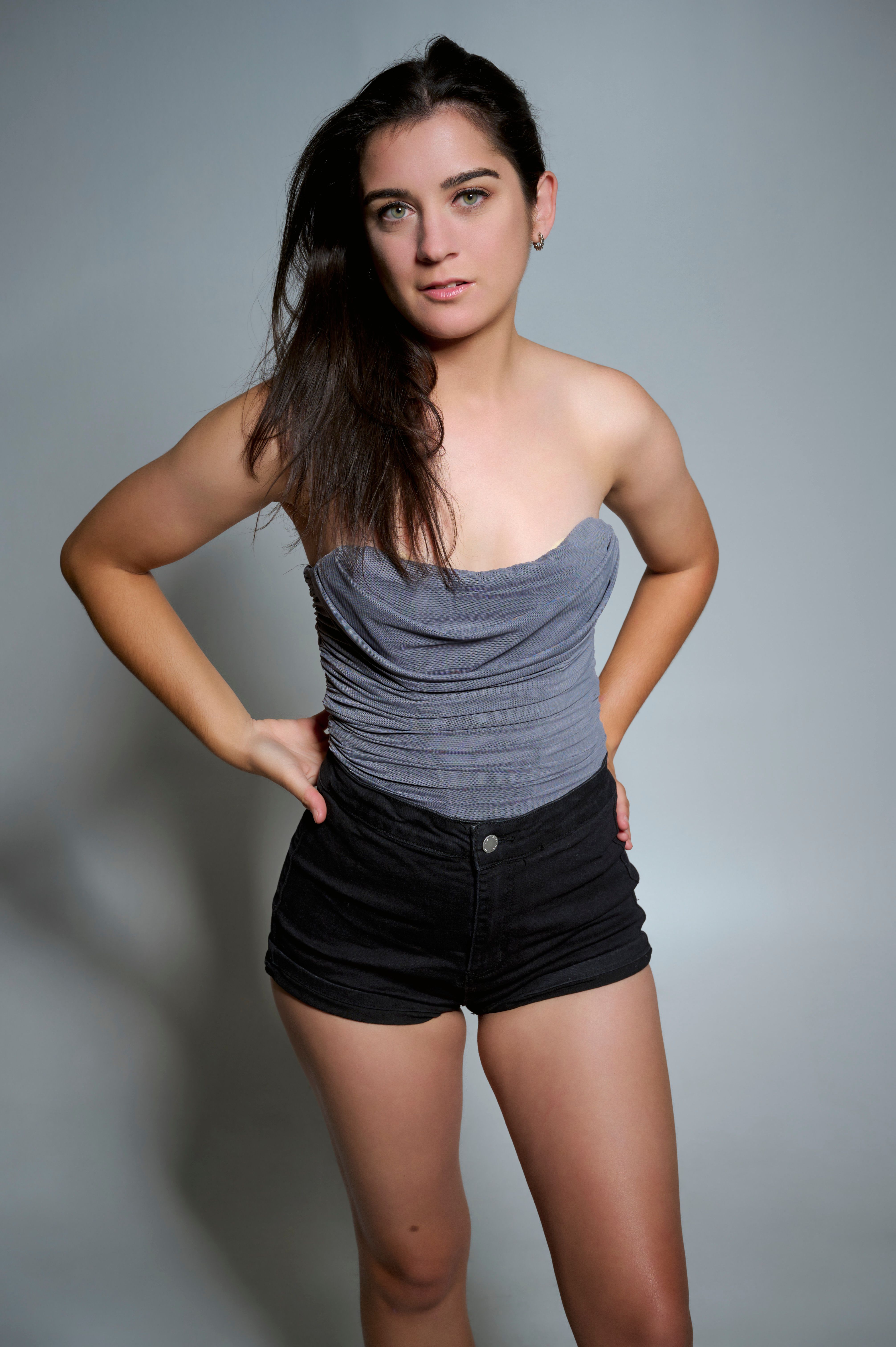 Confident woman posing in gray tube top and black shorts in a studio setting.