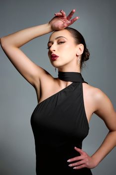 Elegant portrait of a confident woman in black dress on a gray background. Fashion shoot.