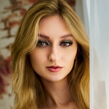 Portrait of a blonde woman with creative makeup and soft lighting indoors.