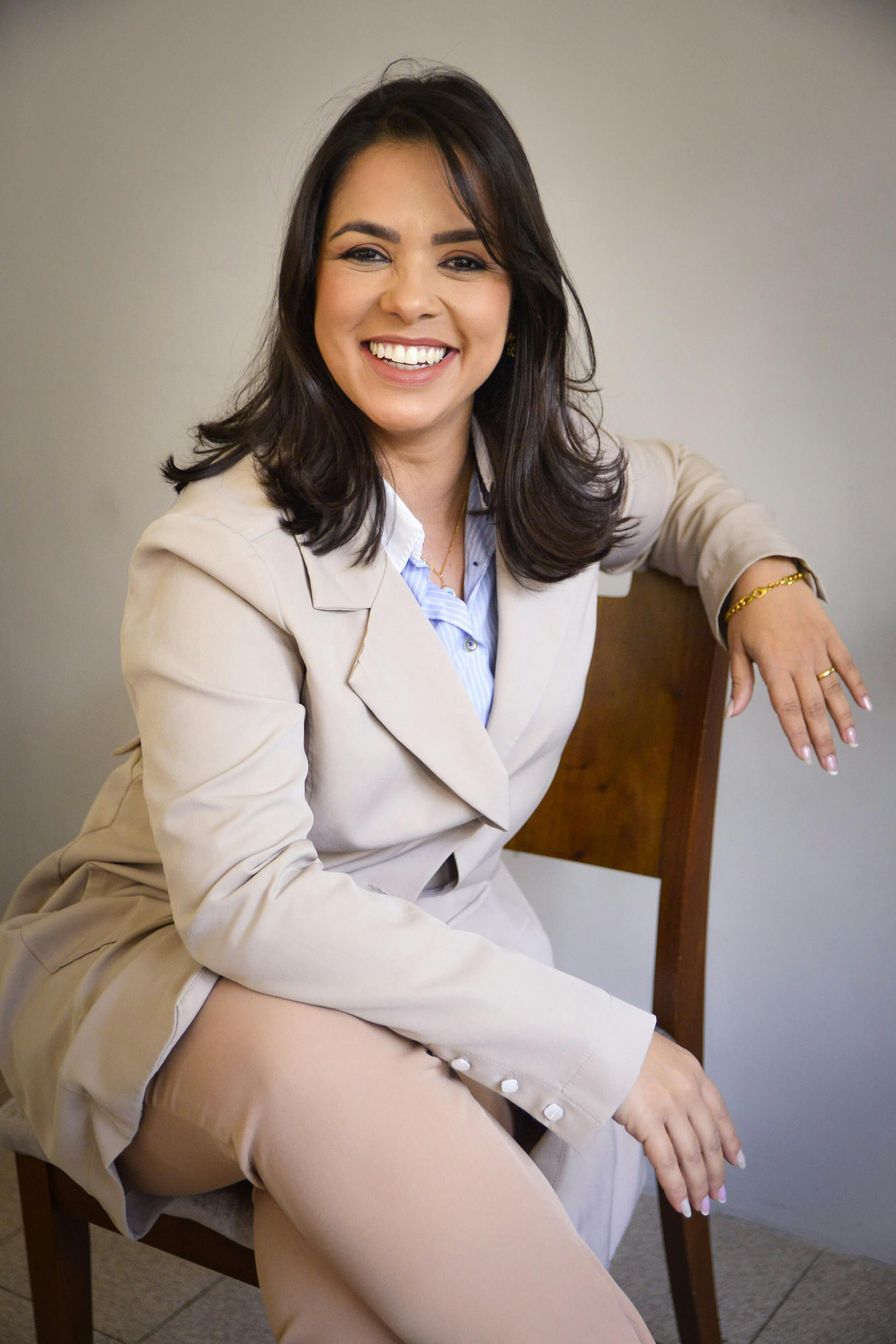 Confident woman sitting and smiling, dressed in a beige suit, symbolizing success and professionalism.