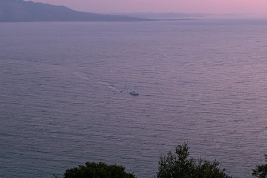 Serene view of the Ionian Sea at sunset with a distant boat and coastal mountains in Sarandë, Albania.