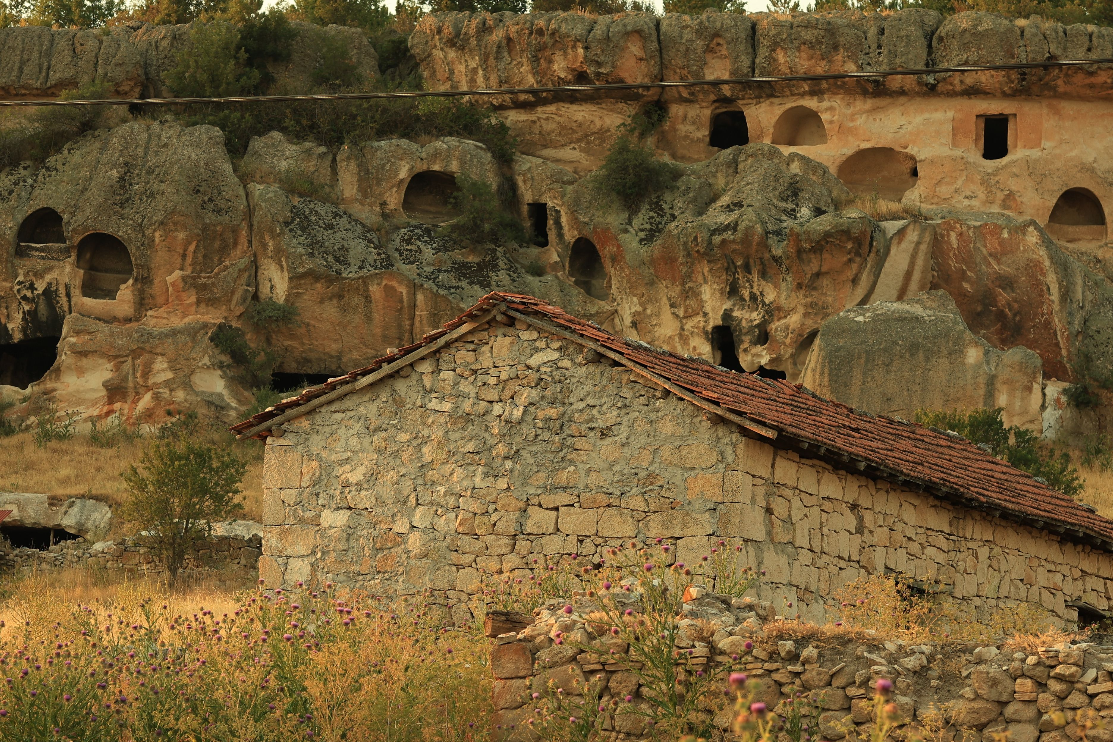 Old stone house in front of ancient rock formations with cave dwellings, Cappadocia, Turkey.