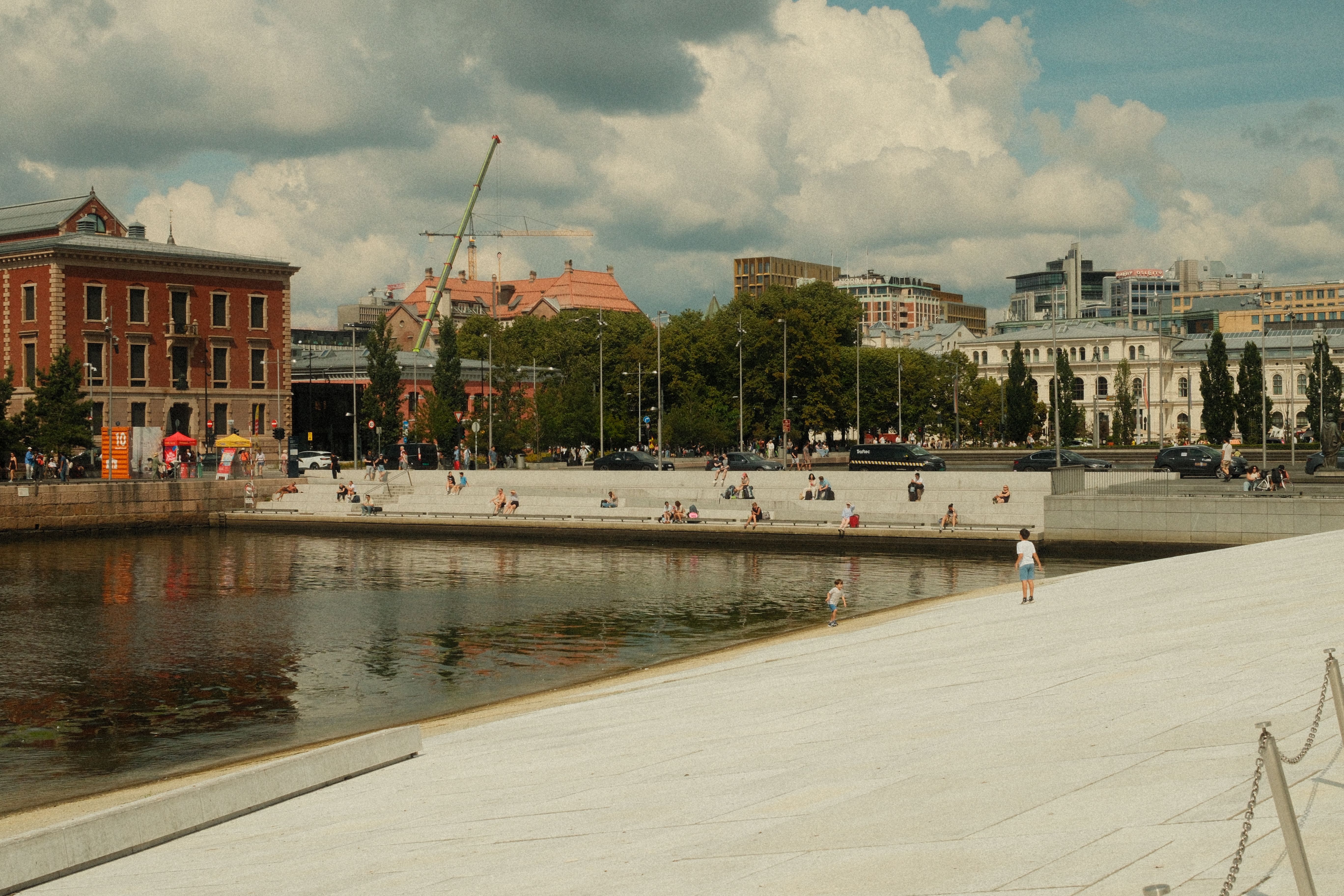 A bustling waterfront plaza in Oslo with people enjoying the sunny day.