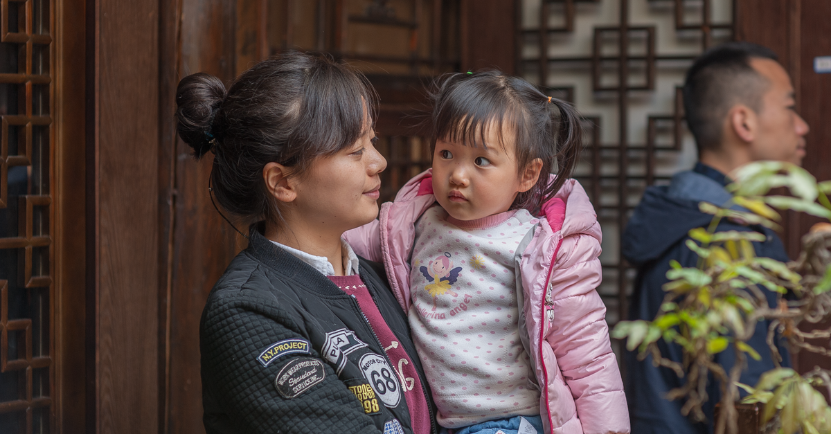 A mother lovingly holds her daughter in a traditional Asian interior.