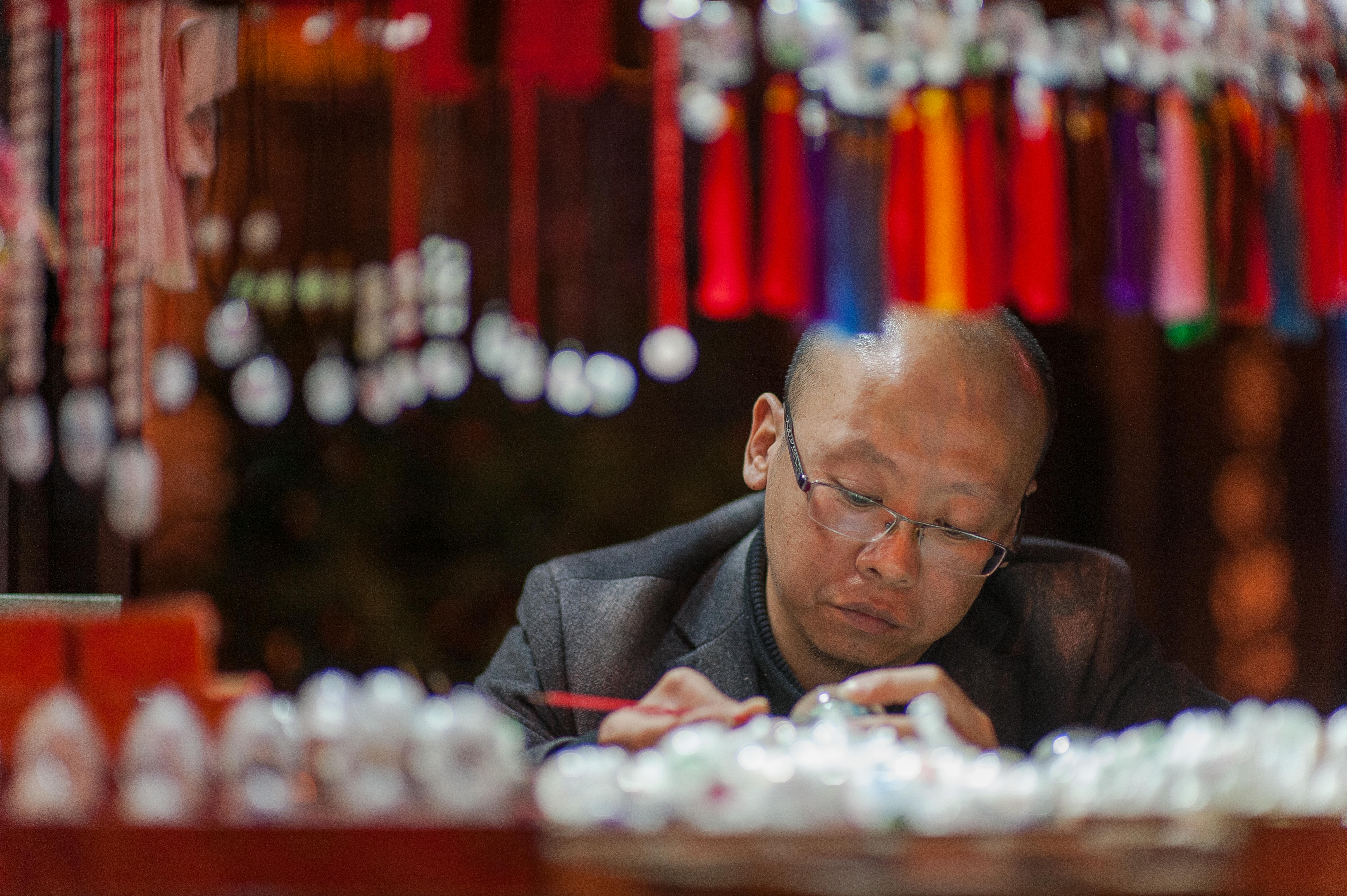 Focused craftsman making handmade jewelry at market with colorful decorations.