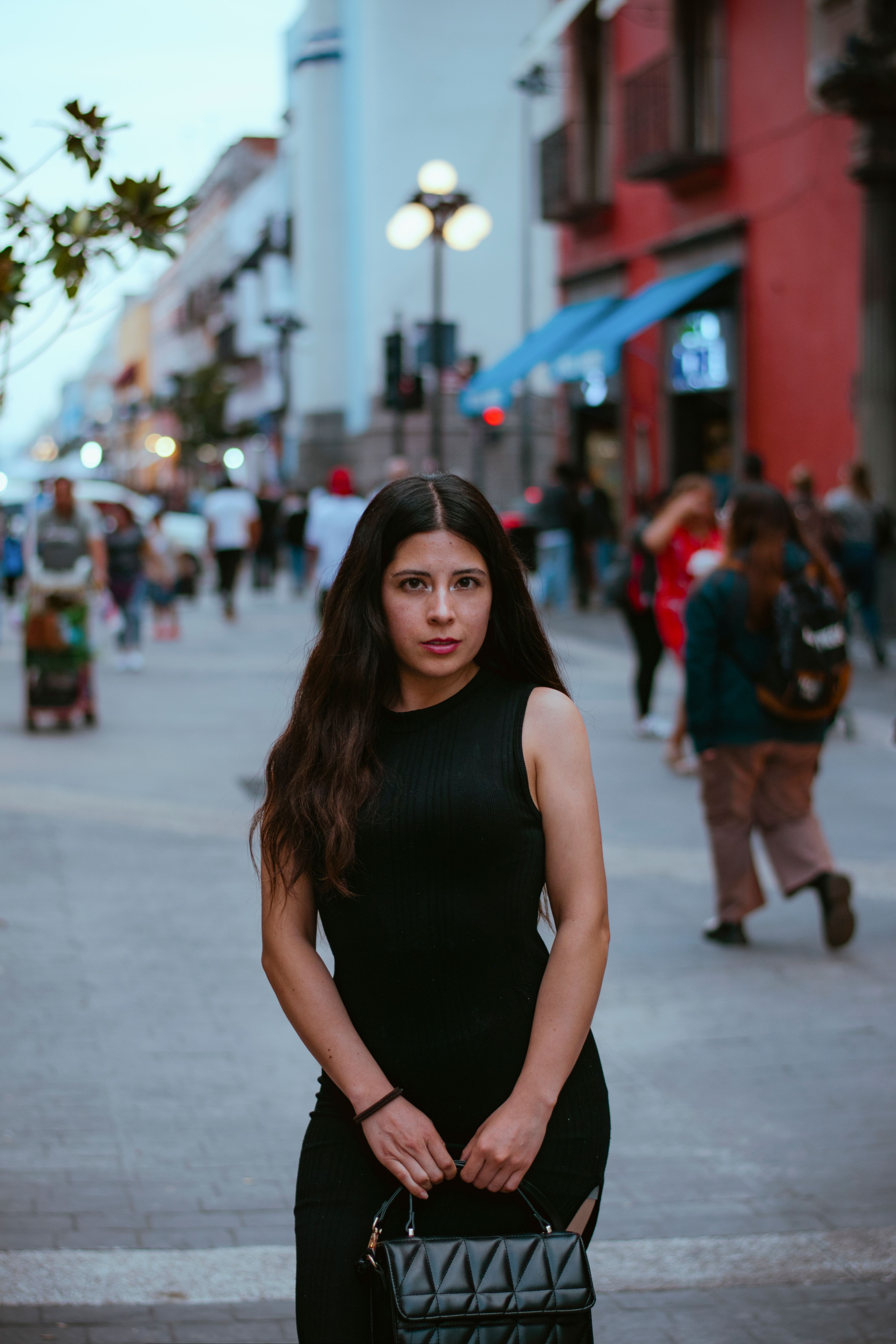 Stylish Woman in Black Dress Stands on Bustling Street · Free Stock Photo