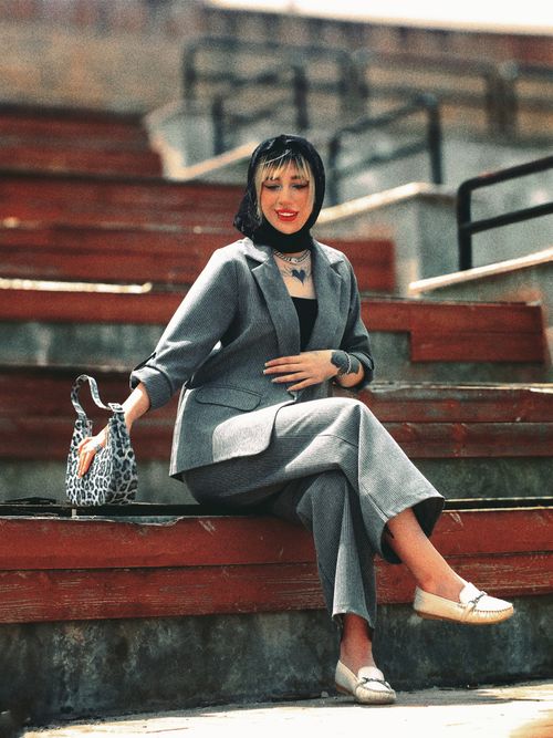 Free Elegant woman in a grey suit sitting on steps outdoors, exuding fashion and confidence. Stock Photo