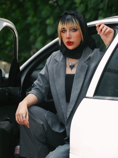 Free A fashionable woman in a pinstripe suit sitting in a car door, exuding confidence and style. Stock Photo