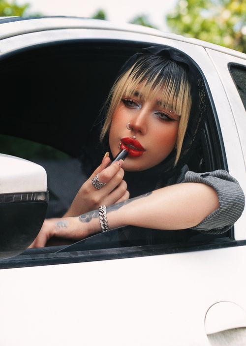 Free Fashionable woman in a car applying bold red lipstick with confidence. Stock Photo