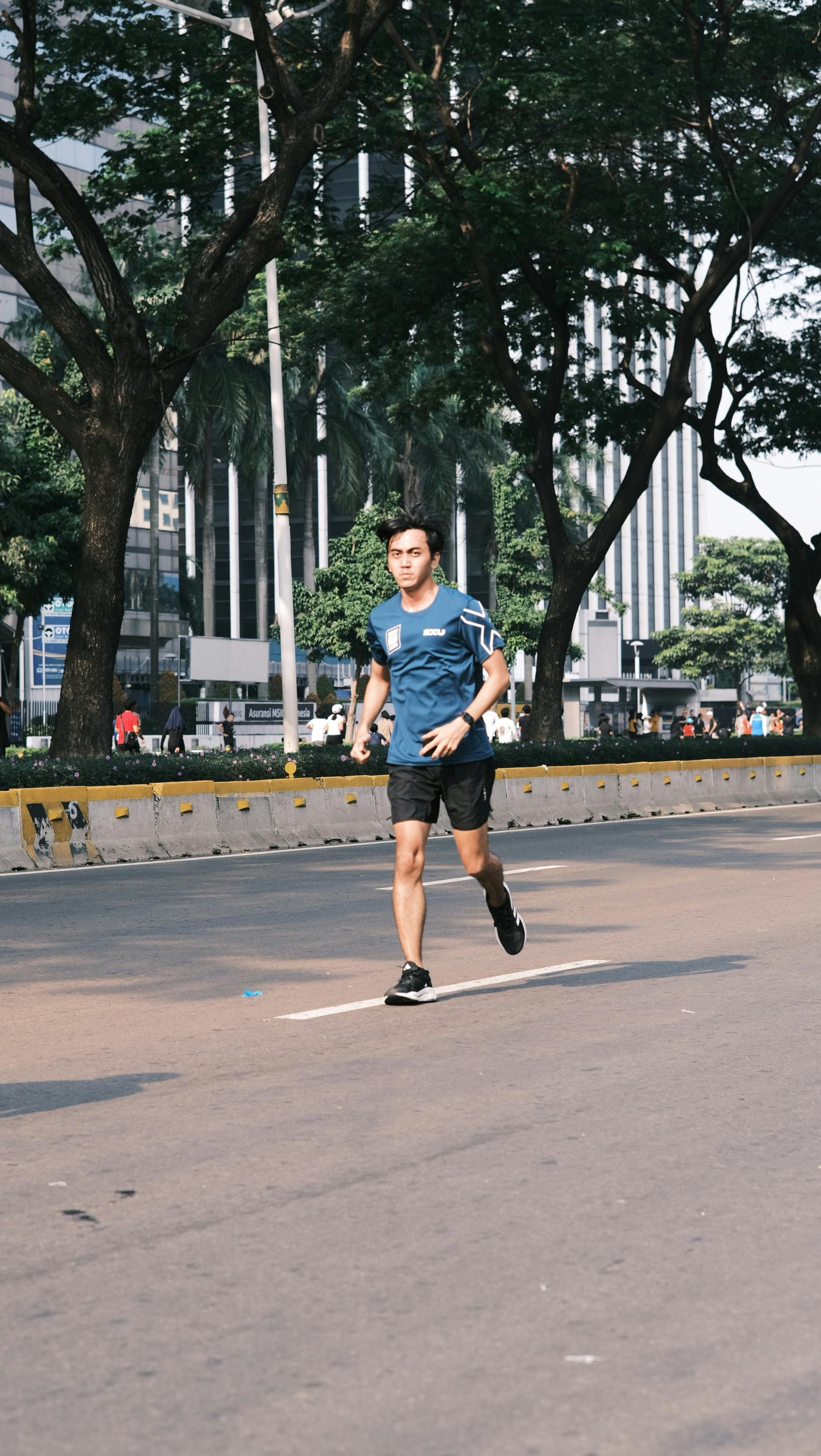 A young man running outdoors on an urban street surrounded by trees during the day.
