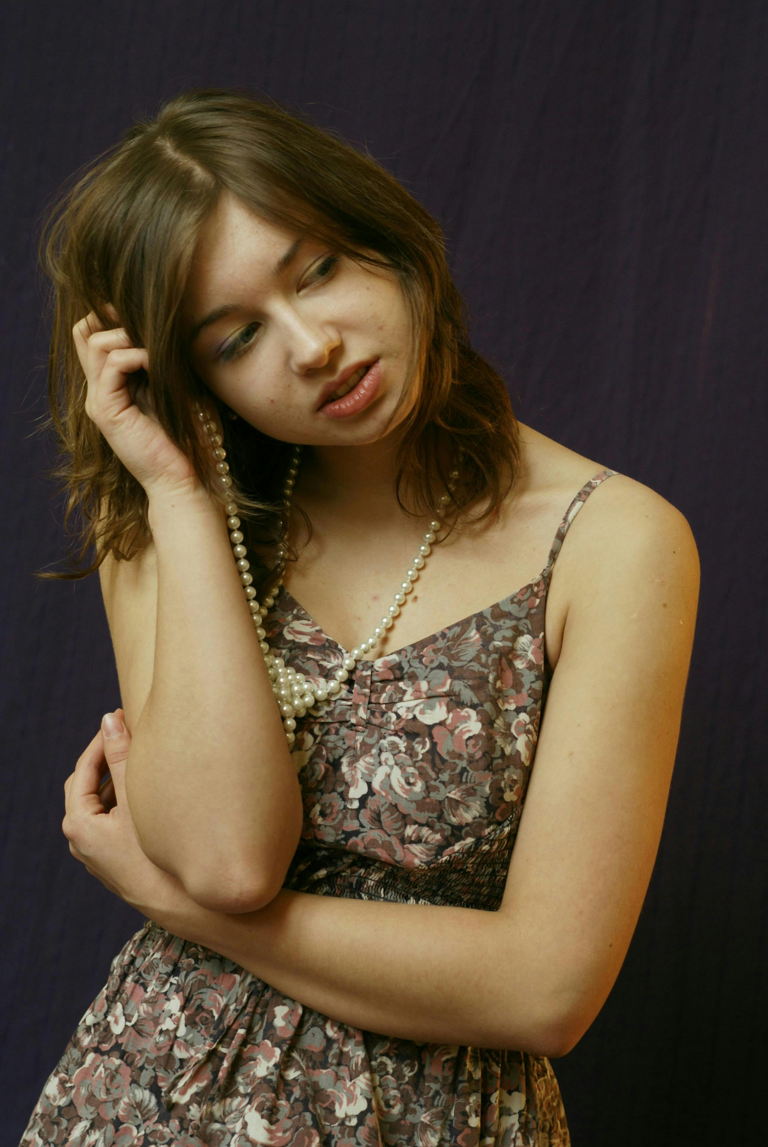 Miễn phí Một phụ nữ trẻ mặc váy hoa và đeo ngọc trai đang tạo dáng một cách trầm ngâm trên nền màu tím. Ảnh lưu trữ