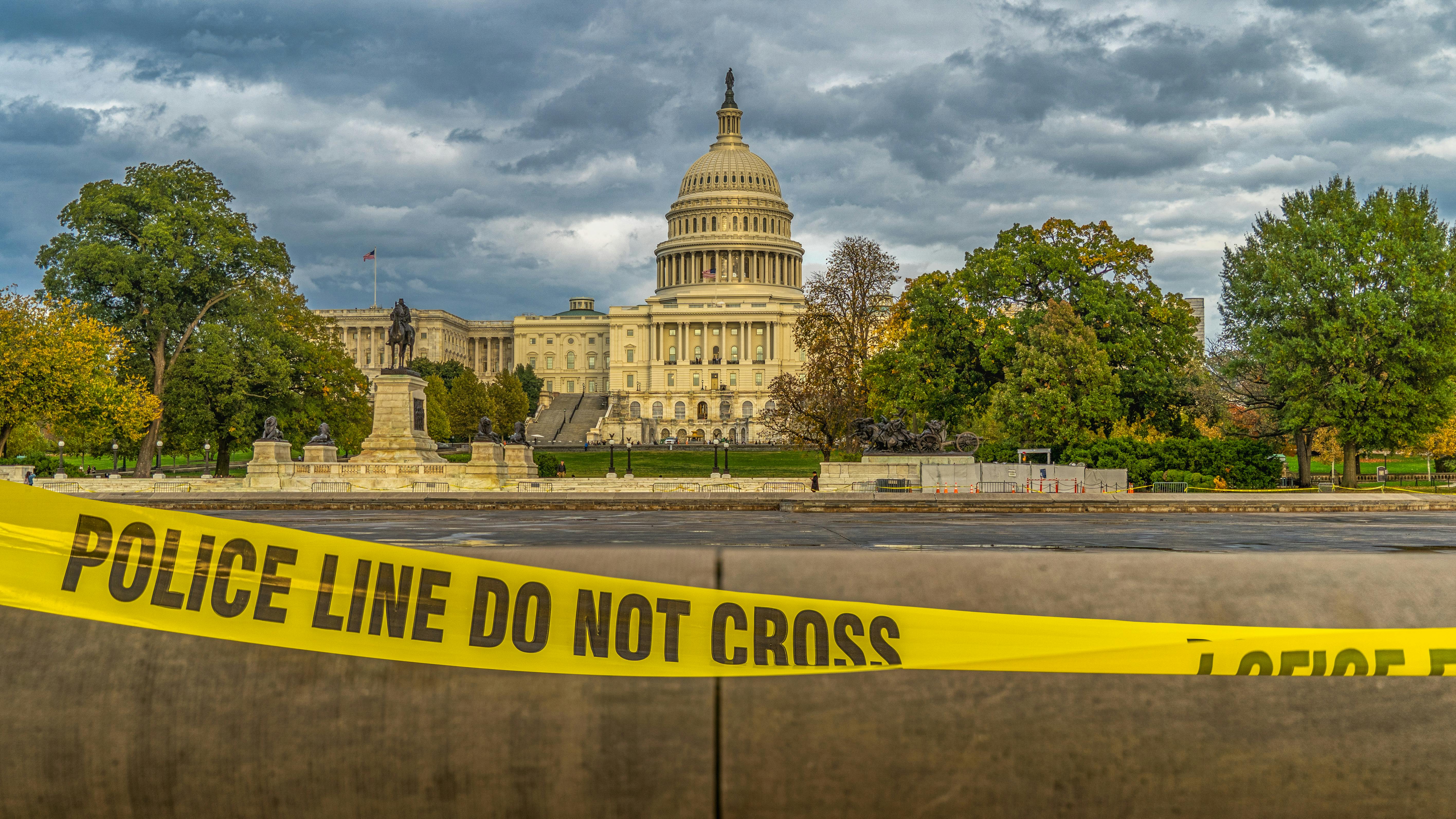 View of US Capitol Building behind police tape under a cloudy sky in Washington, DC.