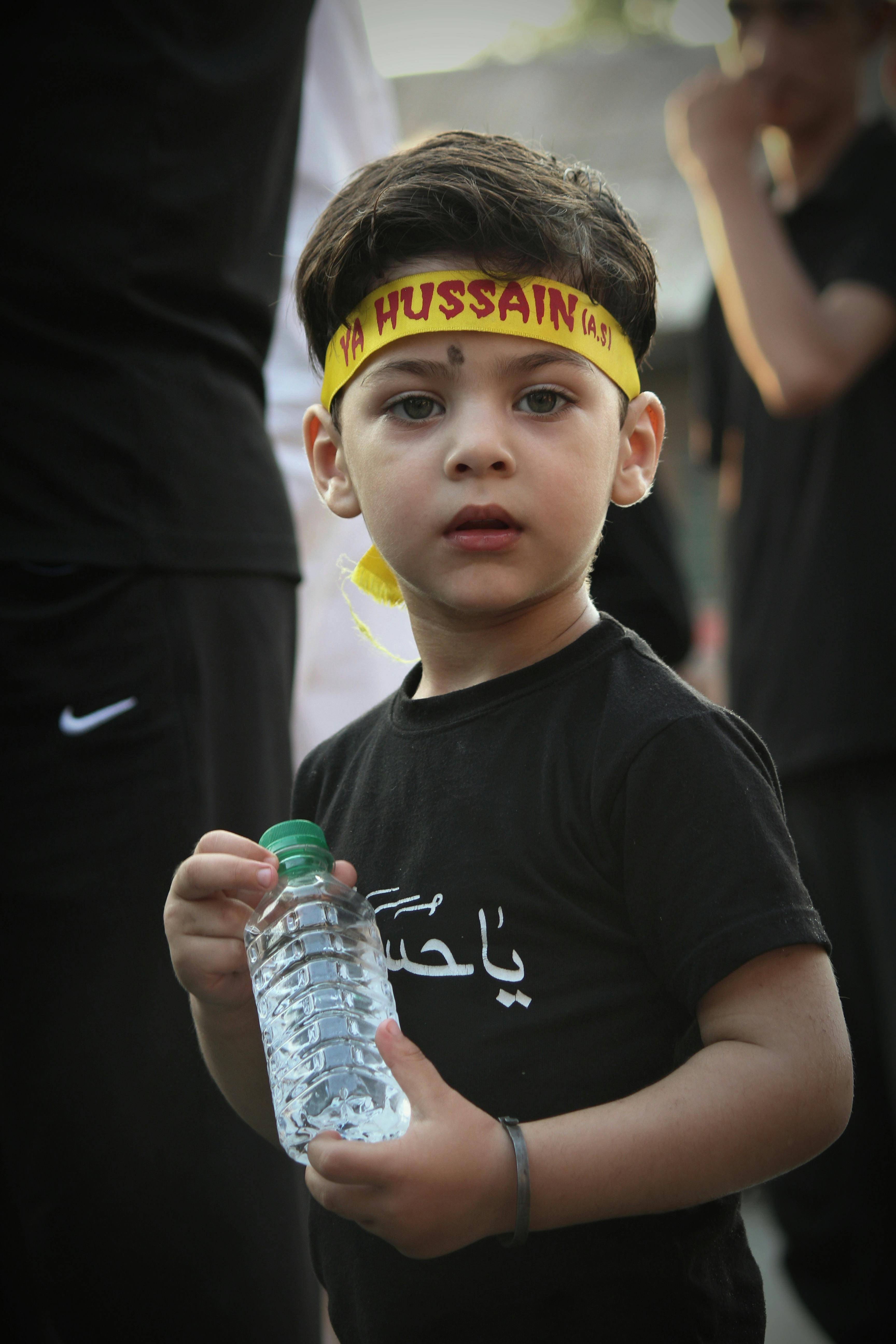 Young boy with headband and water bottle at outdoor religious event, capturing a contemplative moment.