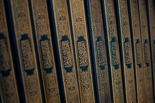 Close-up of Quranic book spines with ornate Arabic calligraphy, showcasing Islamic art and culture.