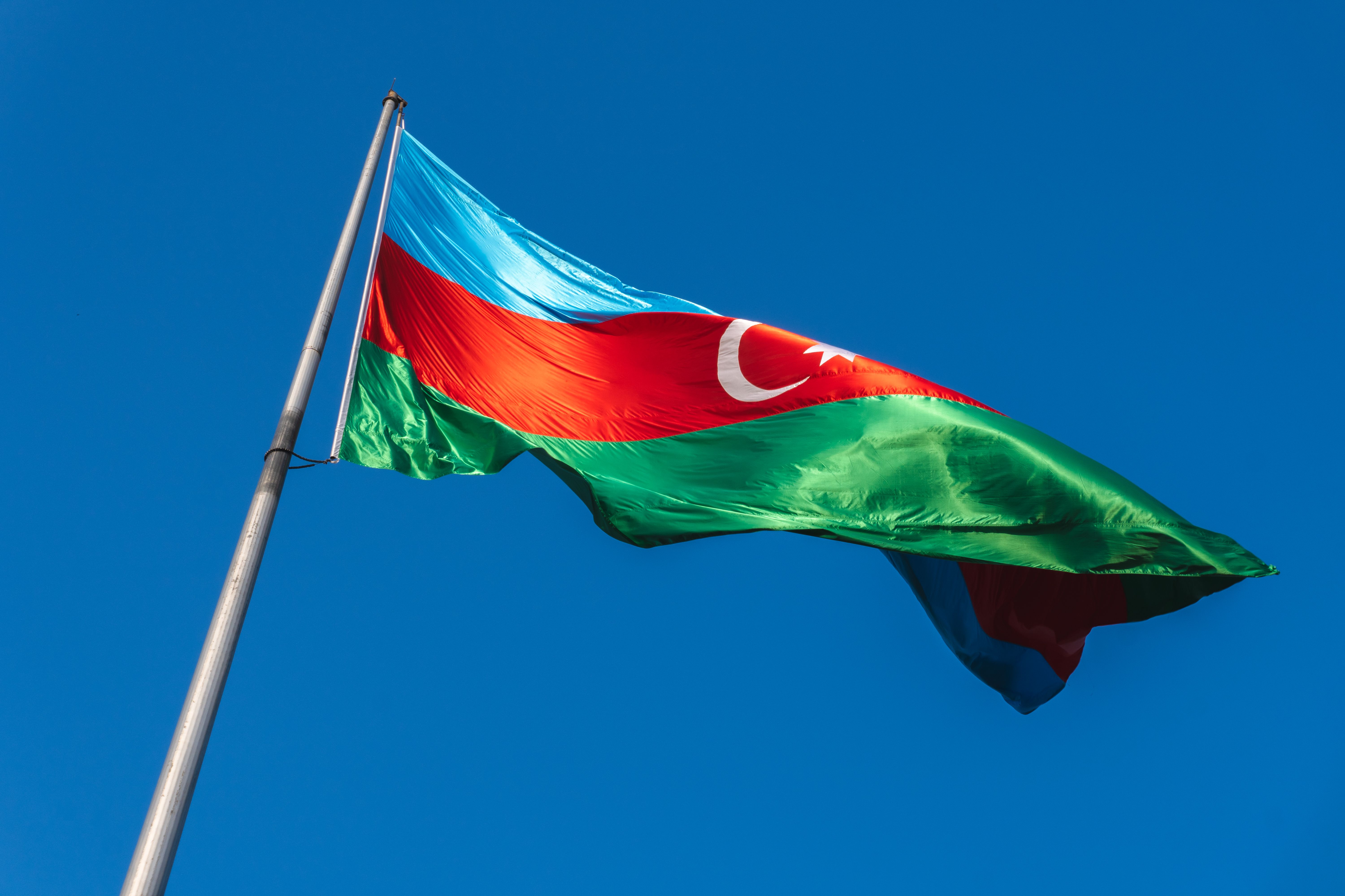 Gratuit Le drapeau national de l'Azerbaïdjan flotte fièrement sur un ciel bleu azur, symbolisant la fierté nationale. Photos
