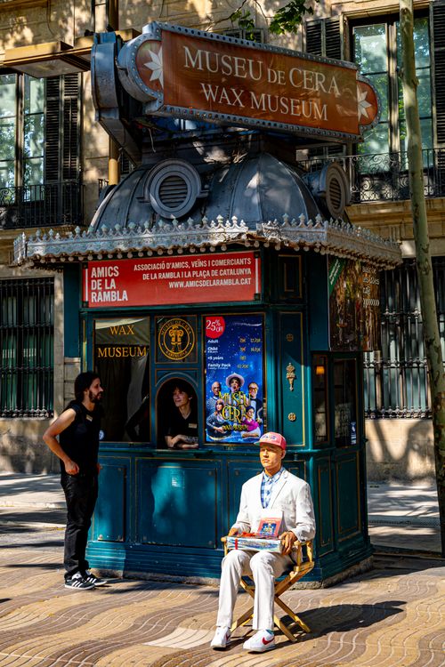 Free Street scene featuring a Barcelona Wax Museum kiosk with people nearby, captured in daylight. Stock Photo